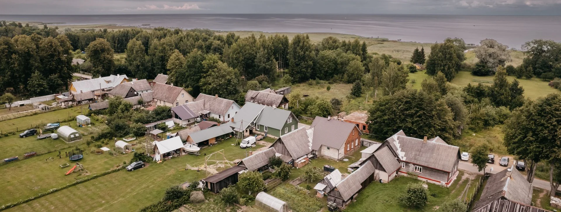 Aerial view of traditional village houses along Lake Peipsi, Estonia, surrounded by green fields and forest with the lake in the background.