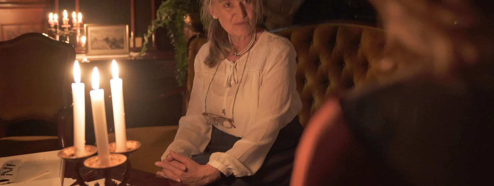Costumed woman sitting by candlelight during a historical storytelling experience in a classic European interior
