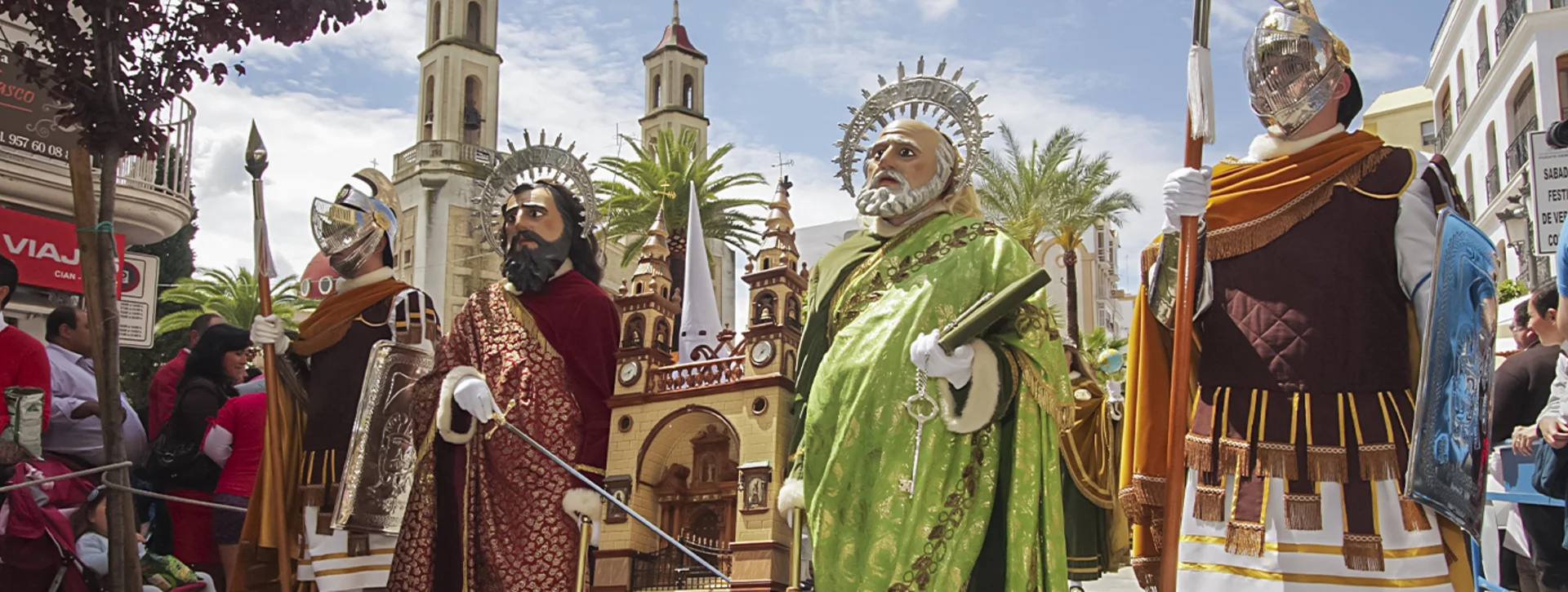 Parade with large religious statues and people in colorful costumes on a sunny day.