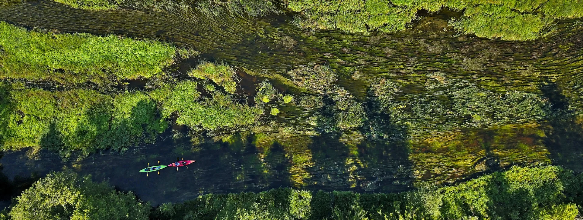 Aerial view of two kayaks on a narrow river surrounded by lush green vegetation.