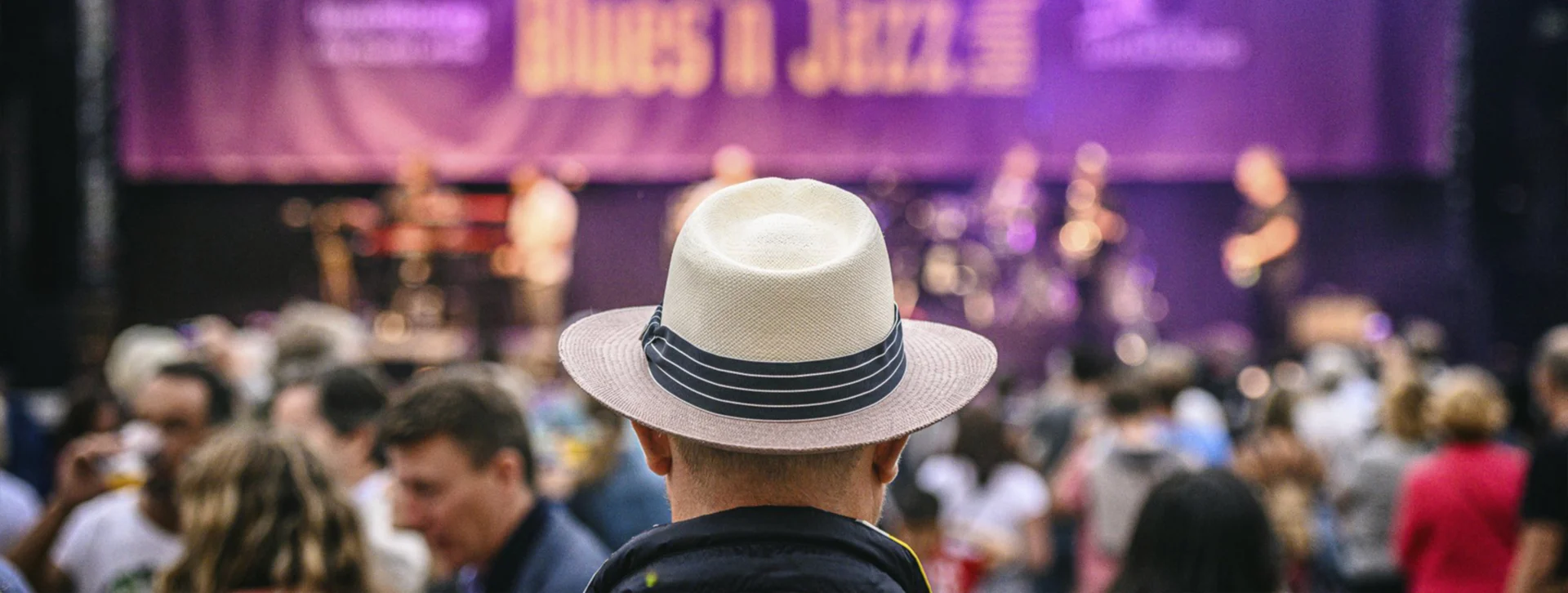 Man in a white hat watching a live band at a crowded outdoor jazz festival.