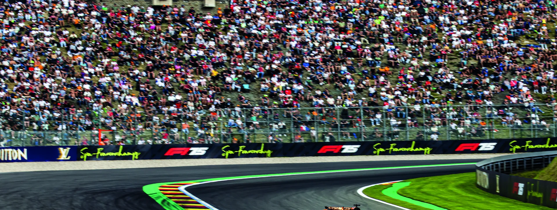 Formula 1 car racing around a track corner, large crowd in the grandstands.