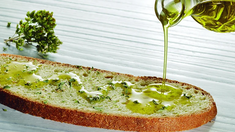 Appreciate the simple magic of rustic bread drizzled with olive oil and sprinkled with fresh herbs, likely oregano, the essence of Mediterranean cuisine.