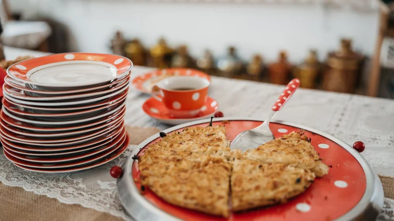 Traditional Estonian onion pie served on a red polka dot plate, next to a stack of matching dishes and a cup of coffee.