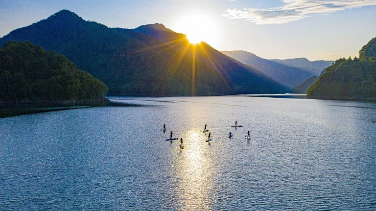 Paddleboarders at sunset on Siriu Lake, framed by forested mountains.