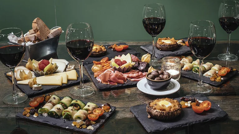 Portuguese petiscos tapas with cheese, charcuterie, vegetables and red wine glasses.
