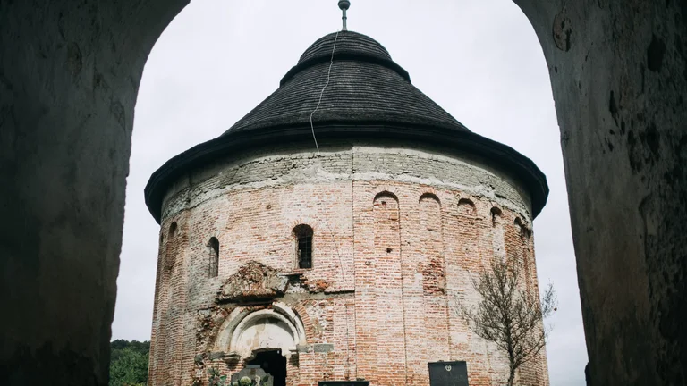 Exterior of the Romanesque rotunda in Sivětice, Slovakia, with graves in front of it on a cloudy day.
