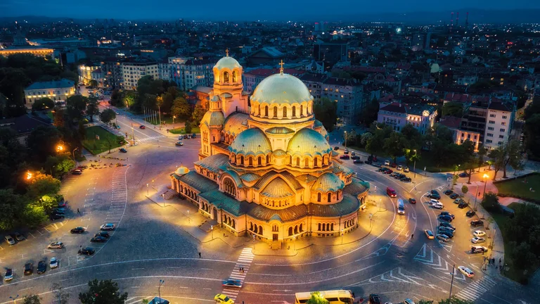 Aerial night view of the Alexander Nevsky Cathedral in Sofia, Bulgaria, illuminated in golden light against the dark cityscape.
