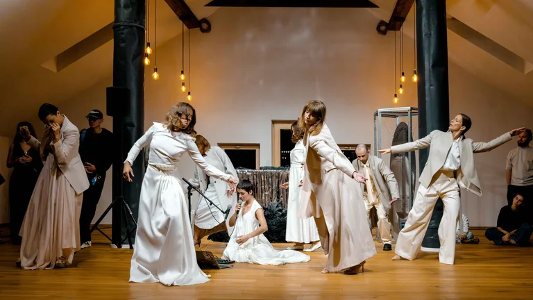 Contemporary dance performance in a loft space with performers wearing white and cream colored clothing, surrounded by minimalist staging.