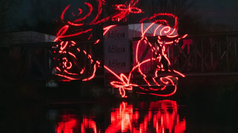 Red light tracing of a scooter shape reflecting clearly on dark water during a night-time light event.