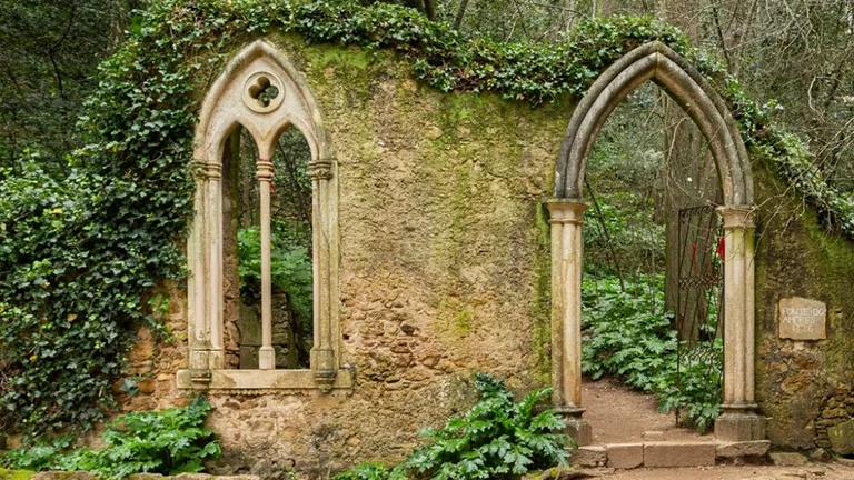 Gothic stone arches in the Gardens of Quinta das Lágrimas, Coimbra, Portugal, surrounded by lush greenery.