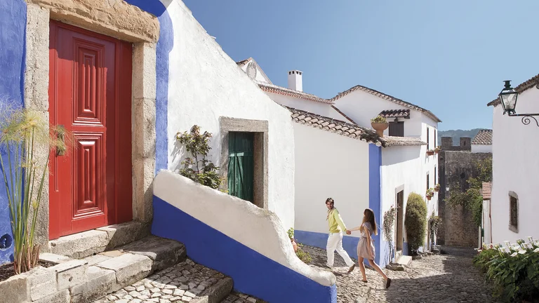 Couple walking through a whitewashed cobbled street in Óbidos.