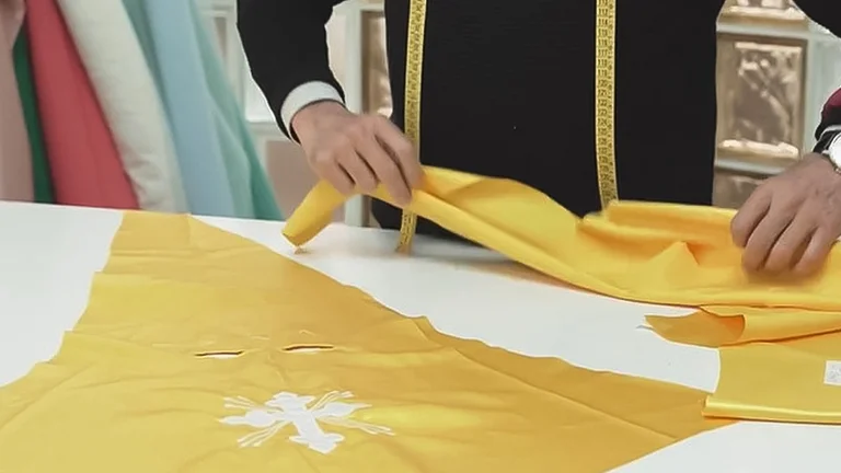 Person measuring yellow fabric with a measuring tape on a white table.