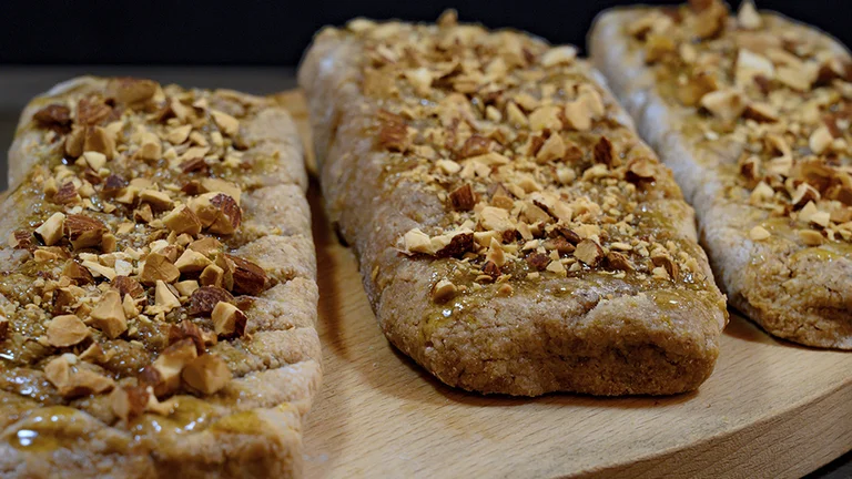 Three rectangular nut-topped pastries on a round wooden board.