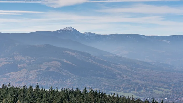 Distant mountain range with a forested foreground under a blue sky with wispy clouds.