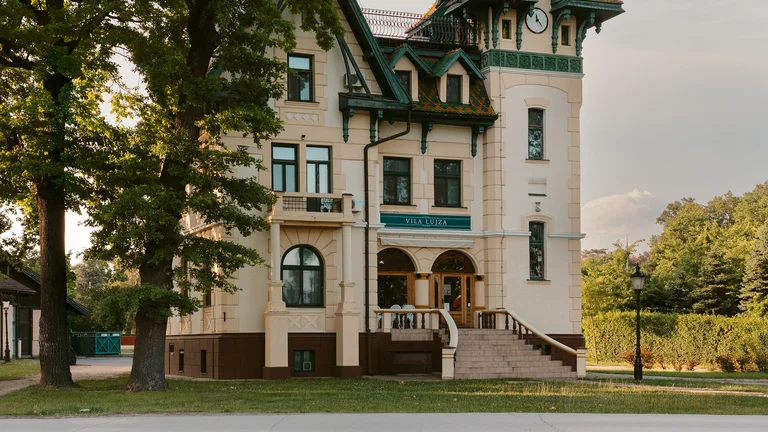 Woman in a hat sitting on grass facing a historic, turreted building with green roof.