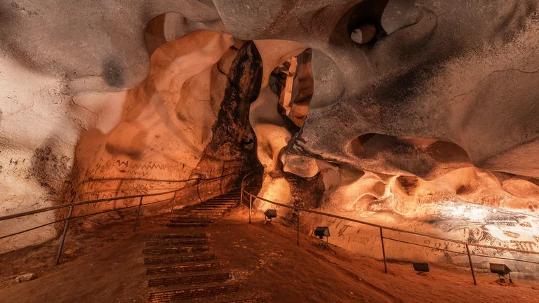 Stairs and railings inside a spacious cave with smooth, orange-lit rock formations.