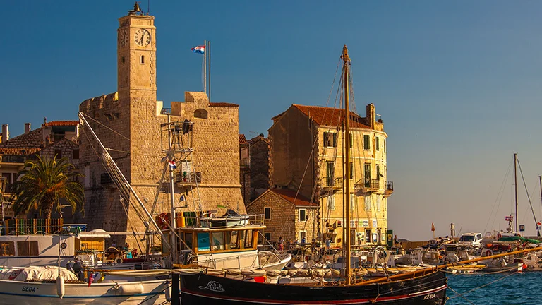 Boats docked by historic stone buildings under a clear blue sky.