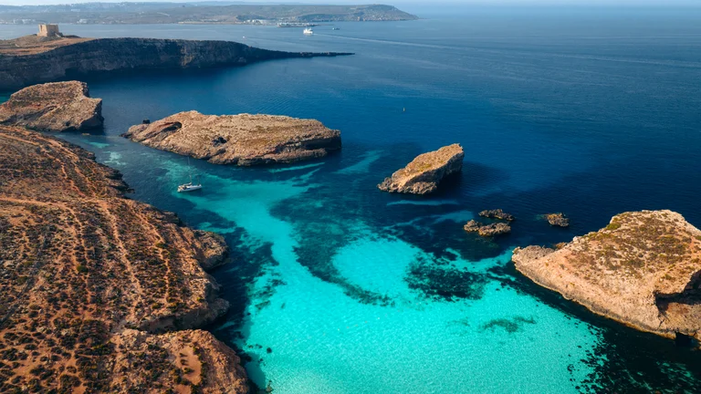 Aerial view of clear blue lagoon surrounded by rocky coastline and islets.