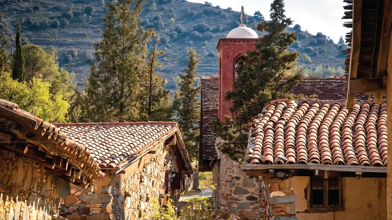 Stone houses with red-tiled roofs, trees, and a red brick tower in a mountain village.