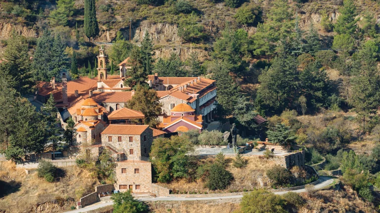 Monastery with red rooftops surrounded by trees and rocky landscape.