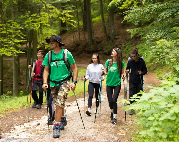 A group of hikers trekking along a rocky mountain path near a high-altitude lake under a clear blue sky.