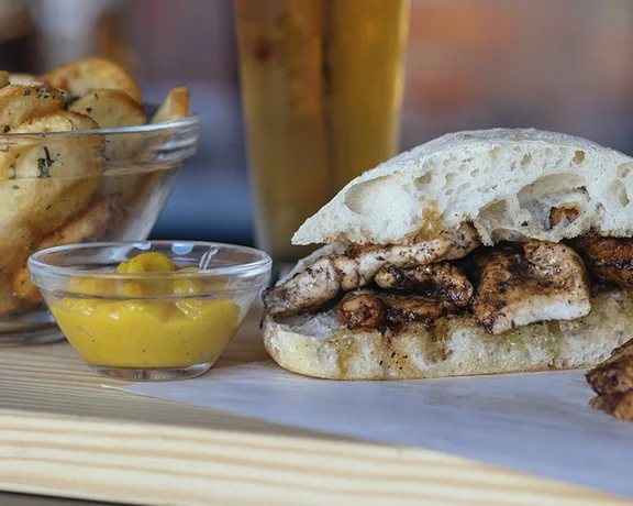 Portuguese bifana pork sandwich served with fried potato slices, mustard and beer.