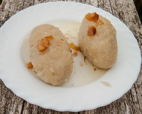 Traditional Podlasie kartacze — potato dumplings filled with meat — served on a plate with fried onions.