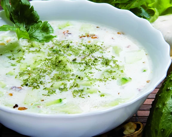 Traditional Bulgarian cold soup called tarator, made with yogurt, cucumbers, garlic, dill, and walnuts, served chilled in a white bowl.