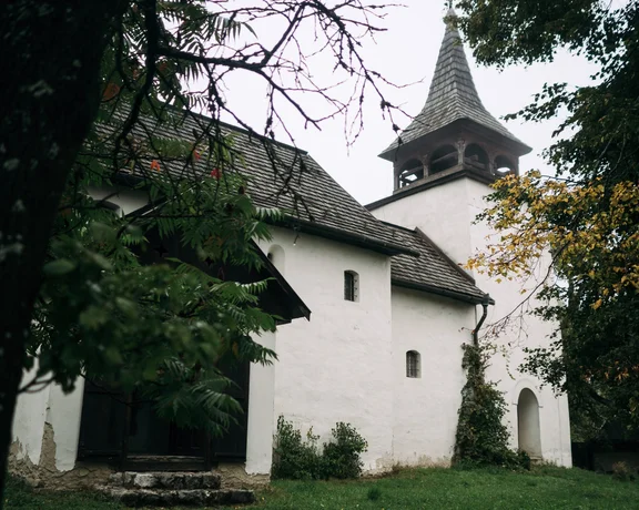Exterior of the Gothic church in Kyjatice, Slovakia, with white walls and a grey pointed roof on a cloudy day.