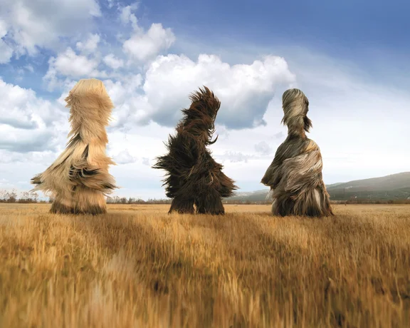 Masked Kukeri dancers in traditional fur costumes with huge bells around their waists, part of a Bulgarian Kukeri festival to scare away evil spirits.