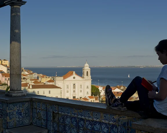 Miradouro de Santa Luzia in Lisbon: a tiled terrace overlooking the red‑rooftops of Alfama and the Tagus River, framed by bougainvillea and historic azulejos