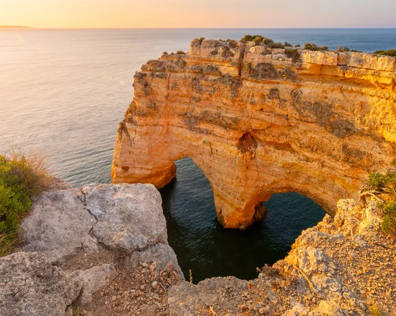 Golden cliffs with sea arch at sunset.