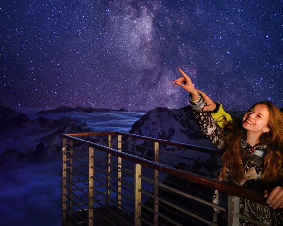Couple stargazing from an observation deck on Lomnický štít in the High Tatras, Slovakia, under a clear night sky and the Milky Way.