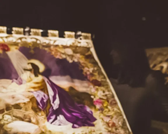 A woman and man admire a brightly lit artwork in a dimly lit gallery.