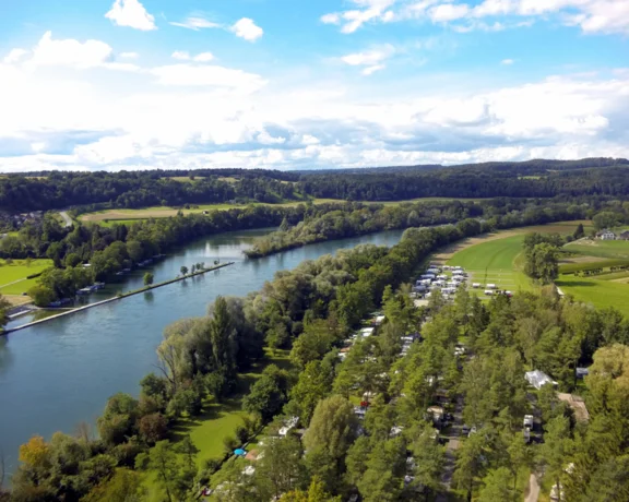 River winding through green fields and trees under a partly cloudy blue sky.