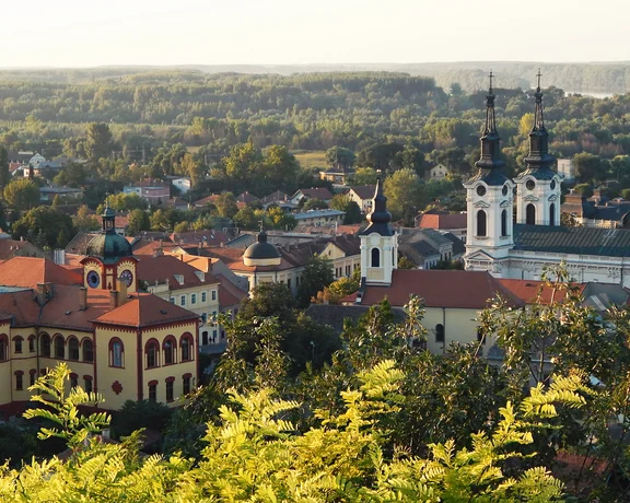 Town with red-roofed buildings and a white church, surrounded by greenery at sunset.