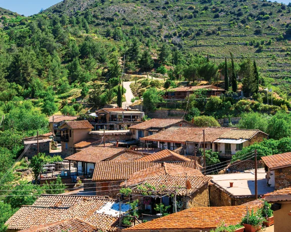 Rustic village with red-tiled roofs surrounded by lush greenery and forested hills.