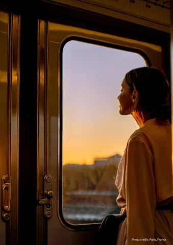 Woman gazing out a train window at sunset, warm sunlight on her face.