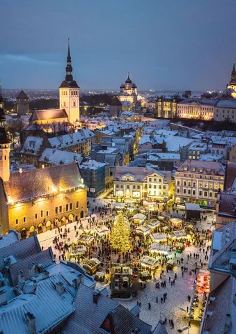 Snowy town square with Christmas market lights and decorated tree at dusk.