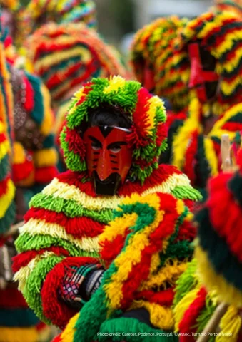 Person in a colorful festival costume with a bright red mask and yarn decorations.