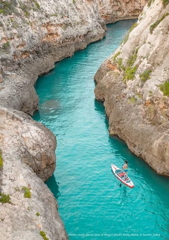 Person paddleboarding on turquoise water between rocky cliffs.