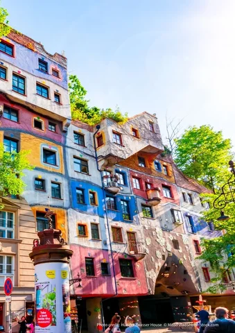 Colorful, uniquely designed apartment building with plants on the roof and people below.