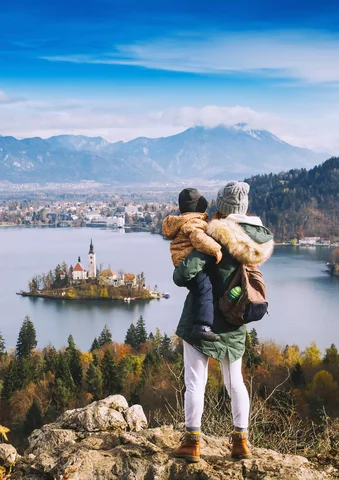 Adult holding a child, overlooking a lake island with mountains in the background.