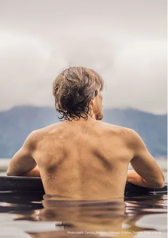 Man with wet hair relaxing in water, facing misty mountains in the distance.