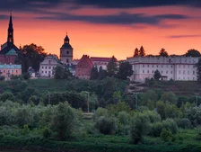 A picturesque town skyline at sunset, featuring historic buildings and a church steeple against a vibrant orange and purple sky.